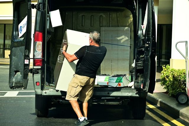 Two workers loading a cabinet into a cargo van