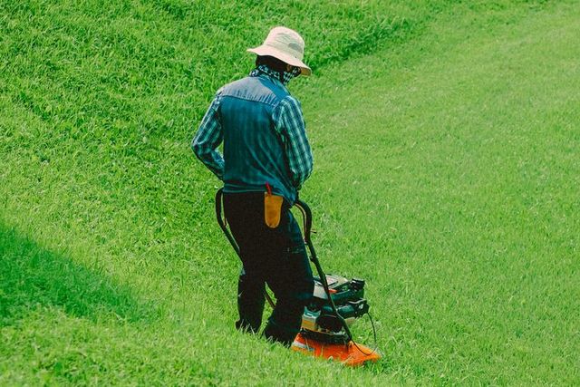 Landscaper mowing a grass slope with a push mower